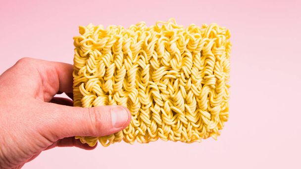 Raw instant noodles in hand on pink background. - Foto, imagen