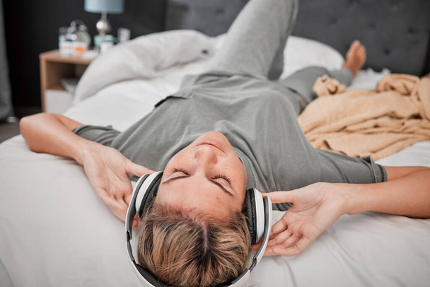 Relájese en la cama, mujer con auriculares y streaming de música en línea. Radio, podcast y contenido para entretenimiento en internet. Chica con tiempo libre escuchando en los auriculares en el dormitorio en casa en paz - Foto, Imagen