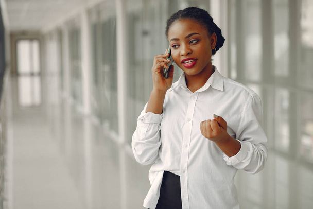 Black girl in the office. Woman in a white shirt. Lady use the phone. - Foto, Bild
