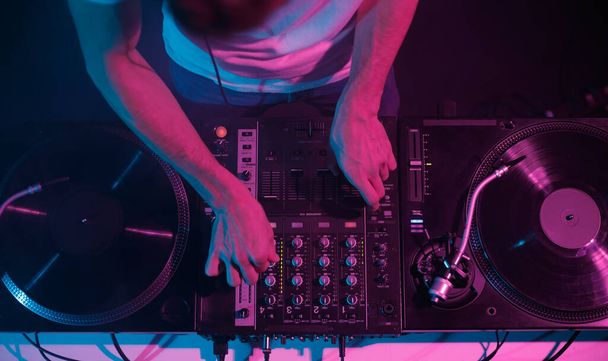 Overhead photo of disc jockey mixing records on party in night club. Professional hip hop DJ plays set on stage, focus on hands - Foto, immagini