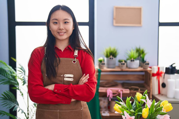Joven florista mujer china sonriendo confiado de pie con los brazos cruzados gesto en la tienda de flores - Foto, Imagen