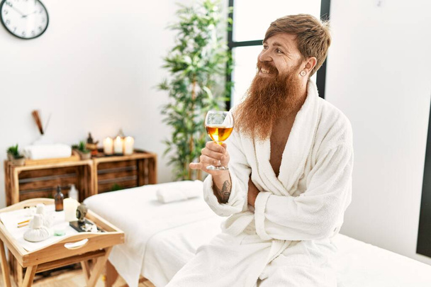 Молодий рудий чоловік в халаті п'є шампанське в центрі краси
 - Фото, зображення