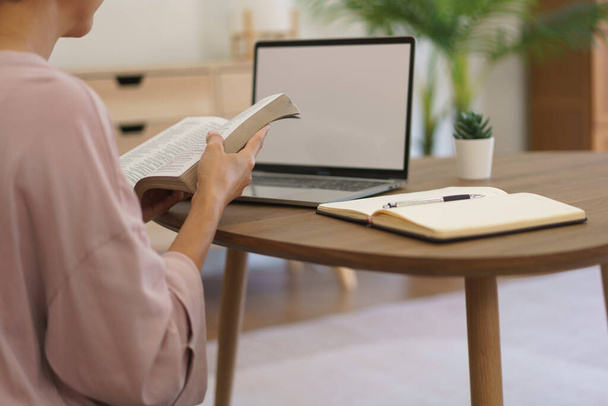 Female entrepreneur reading a literature book to relaxation after working on laptop at home. - Photo, Image