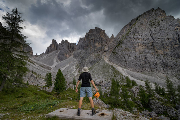 Ein Mann steht mit einem Helm in der Hand und bewundert die Gipfel der Dolomiten. Dolomiten, Italien - Foto, Bild