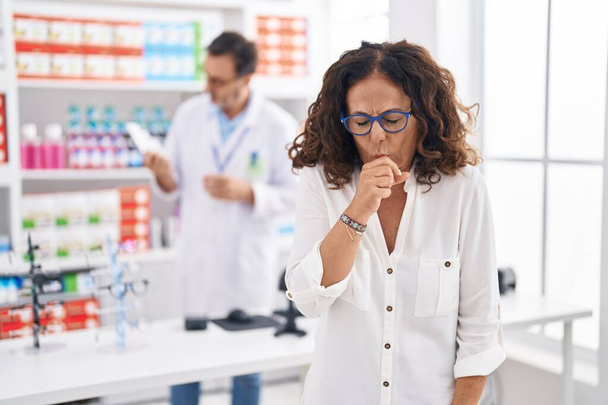 Femme hispanique d'âge moyen faisant ses courses à la pharmacie se sentant mal et toussant comme symptôme du rhume ou de la bronchite. concept de soins de santé.  - Photo, image