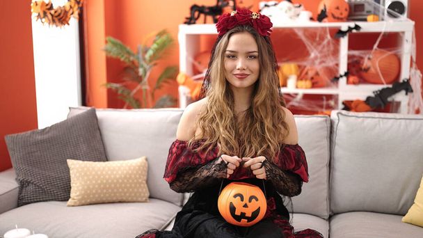 Young beautiful hispanic woman wearing katrina costume holding halloween pumpkin basket at home - Foto, Imagen