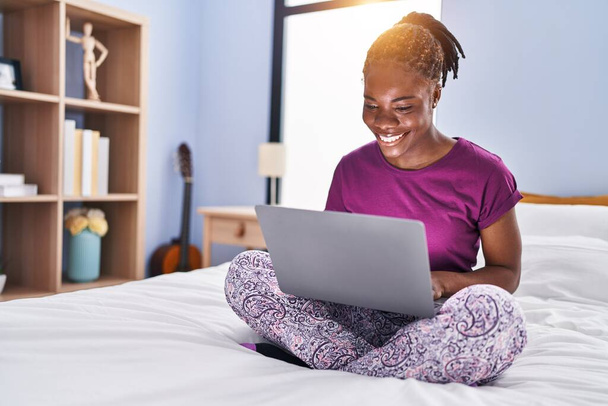 Afrikai amerikai nő laptoppal ül az ágyon a hálószobában - Fotó, kép