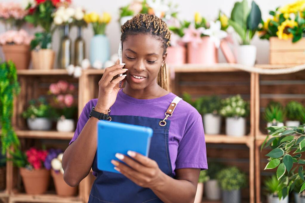 Afrikkalainen amerikkalainen nainen kukkakauppa puhuu älypuhelimella käyttäen kosketuslevy at kukkakauppa - Valokuva, kuva