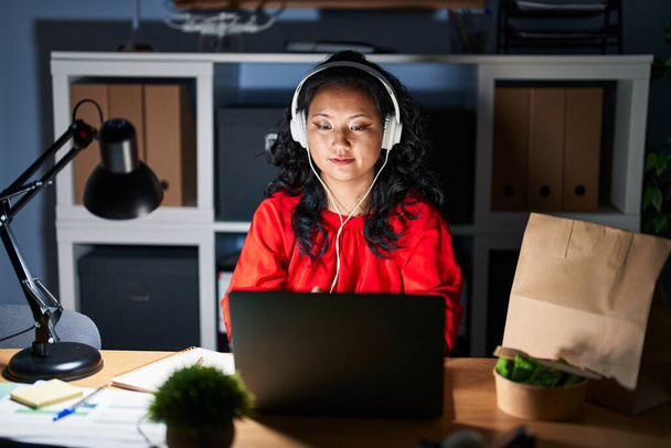 真夜中にノートパソコンで事務所で働く若いアジア人女性が真剣な表情でリラックス。カメラを見ているだけで.  - 写真・画像