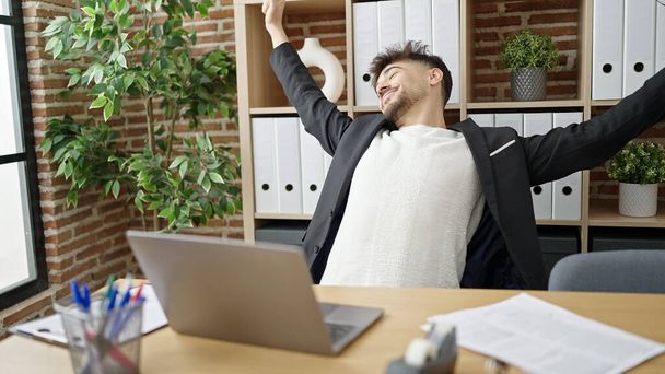 Молодой арабский бизнесмен использует ноутбук, растягивающий руки в офисе - Фото, изображение