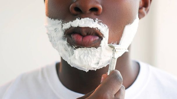 Face shaving. Male grooming. Facial hygiene. Closeup of unrecognizable man with white moisturizing skin foam cream beard using sharp razor blade. - Photo, Image