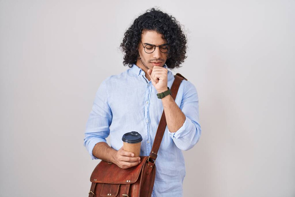 Hispanic man with curly hair drinking a cup of take away coffee feeling unwell and coughing as symptom for cold or bronchitis. health care concept.  - 写真・画像