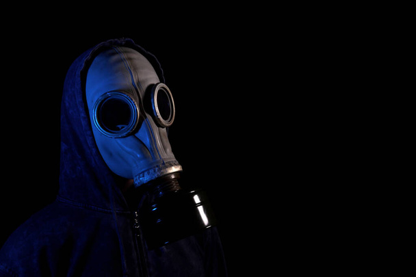 Man in a hood in an old retro gas mask in neon light on a black background - Фото, изображение