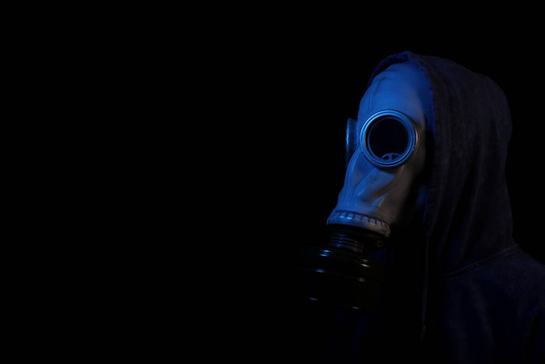 Mann mit Kapuze in einer alten Retro-Gasmaske in Neonlicht auf schwarzem Hintergrund - Foto, Bild