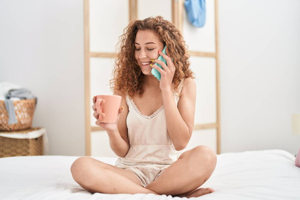 Junge schöne hispanische Frau spricht auf Smartphone und trinkt Kaffee im Schlafzimmer - Foto, Bild