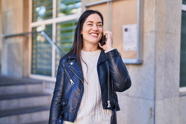 Junge Frau lächelt selbstbewusst und spricht auf der Straße mit dem Smartphone - Foto, Bild