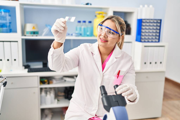 Young hispanic woman wearing scientist uniform looking sample at laboratory - Photo, Image