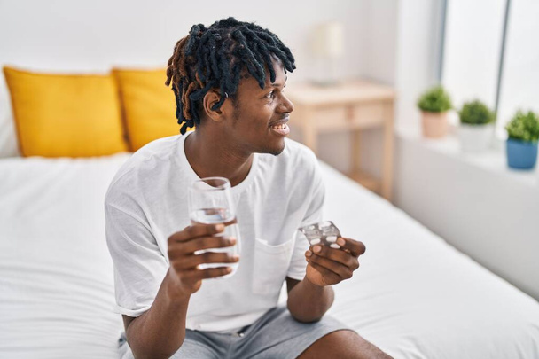 Afro-Amerikaanse man neemt pillen zittend op bed in de slaapkamer - Foto, afbeelding