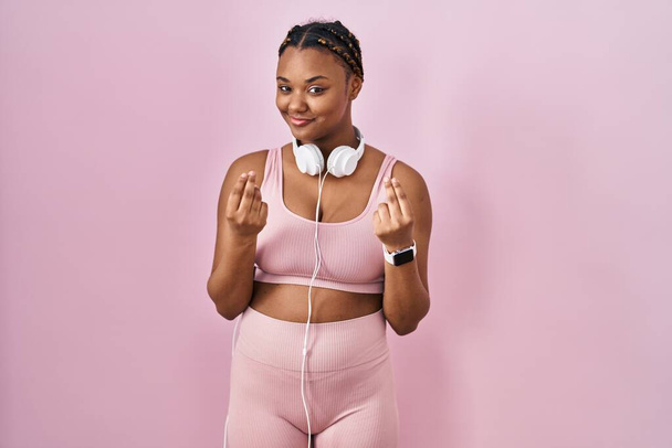 African american woman with braids wearing sportswear and headphones doing money gesture with hands, asking for salary payment, millionaire business  - Фото, изображение
