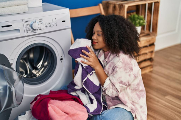 Νεαρή Αφροαμερικανή γυναίκα χαμογελά με αυτοπεποίθηση πλύσιμο ρούχων στο πλυντήριο - Φωτογραφία, εικόνα