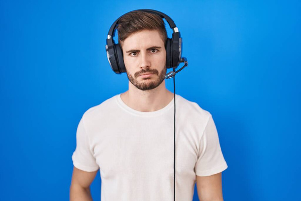 Hispanic man with beard listening to music wearing headphones depressed and worry for distress, crying angry and afraid. sad expression.  - Photo, Image