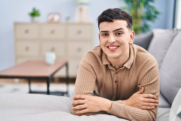 Young non binary man smiling confident lying on sofa at home - Foto, imagen