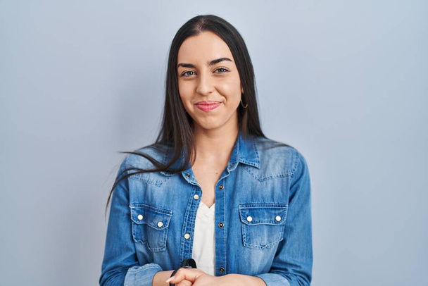 Hispanic woman standing over blue background with hands together and crossed fingers smiling relaxed and cheerful. success and optimistic  - Valokuva, kuva