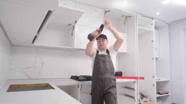 非常に明るいキッチン家具のインストーラは、作業ツールで踊ります。仕事で幸せな従業員 - 映像、動画