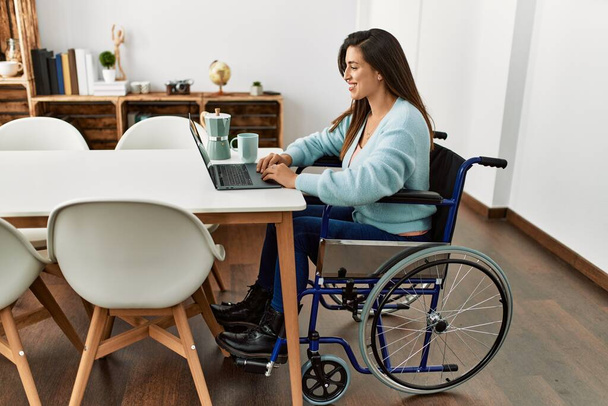 Молодая женщина с ноутбуком сидит на инвалидной коляске работает на дому - Фото, изображение