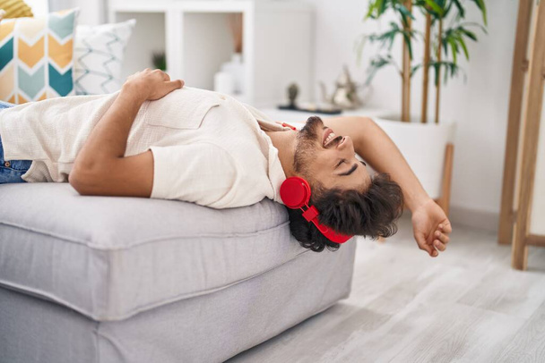 Молодой араб слушает музыку, лежащую дома на диване - Фото, изображение
