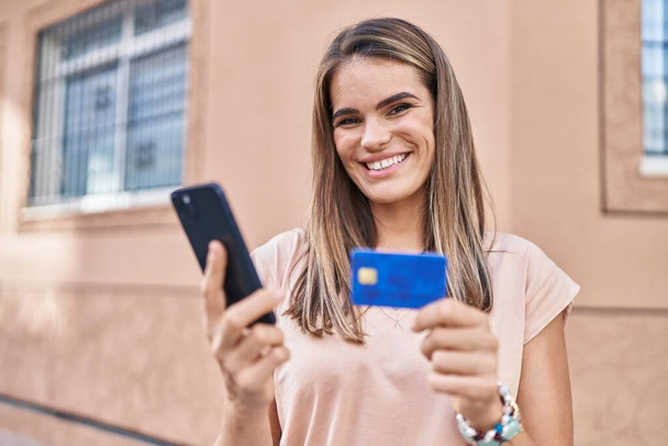 Joven mujer hispana hermosa usando teléfono inteligente y tarjeta de crédito en la calle - Foto, imagen