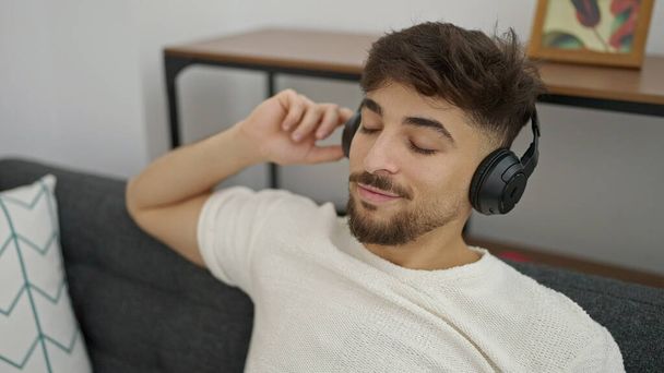 Mladý arabský muž poslouchá hudbu sedí na pohovce doma - Fotografie, Obrázek