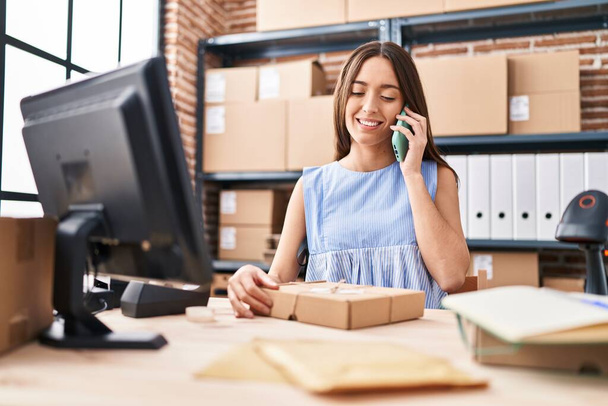 Молода красива іспанська жінка електронної комерції бізнесмен розмовляє на смартфоні тримаючи пакет в офісі
 - Фото, зображення