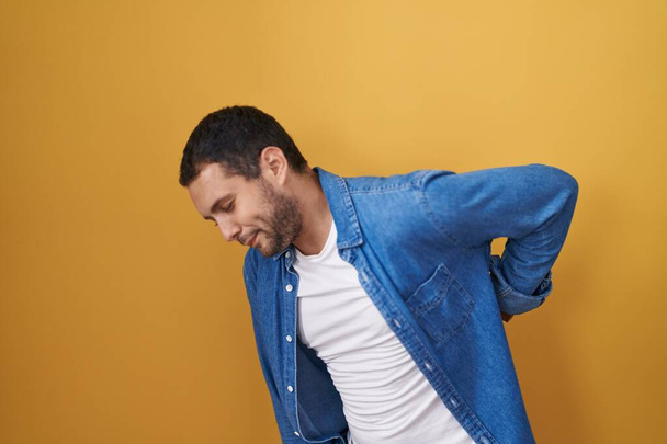 Hispanic man standing over yellow background suffering of backache, touching back with hand, muscular pain  - Foto, afbeelding