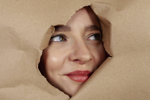 Close up: A girl's face is peeking out from a cutout in a large sheet of kraft paper. - Foto, immagini