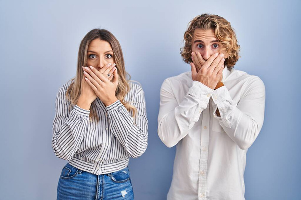 Young couple standing over blue background shocked covering mouth with hands for mistake. secret concept.  - Φωτογραφία, εικόνα