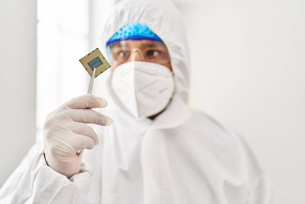 Молодой латиноамериканец ученый в защитной униформе с процессорным чипом в лаборатории - Фото, изображение