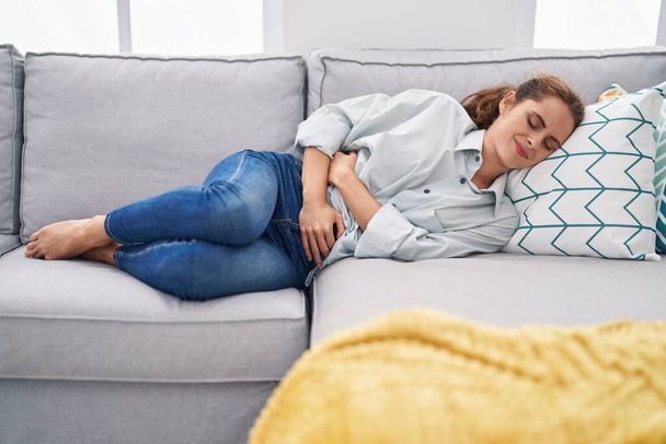 Nuori nainen kärsii kuukautiskivusta makaa sohvalla kotona - Valokuva, kuva