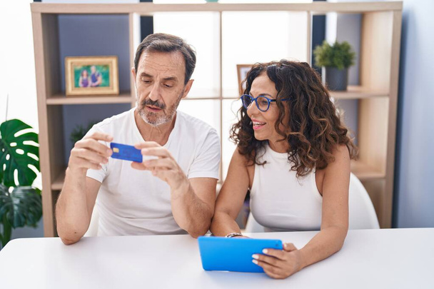 Kadın ve erkek, evdeki masada oturan dokunmatik kağıt ve kredi kartı kullanıyorlar. - Fotoğraf, Görsel