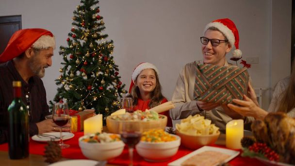メリークリスマス、クリスマスギフトボックス付きの大きな家族、一緒にクリスマスの日を祝うサンタの帽子を持つ幸せな人々、クリスマスのお祝いのコンセプトを持つ家族 - 写真・画像