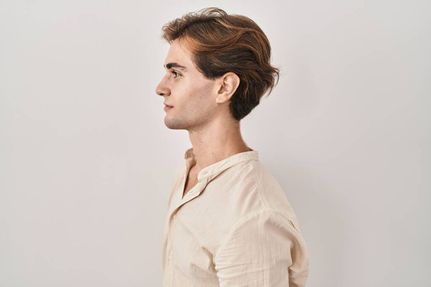 Jeune homme debout sur fond isolé regardant vers le côté, pose de profil relax avec le visage naturel et sourire confiant.  - Photo, image