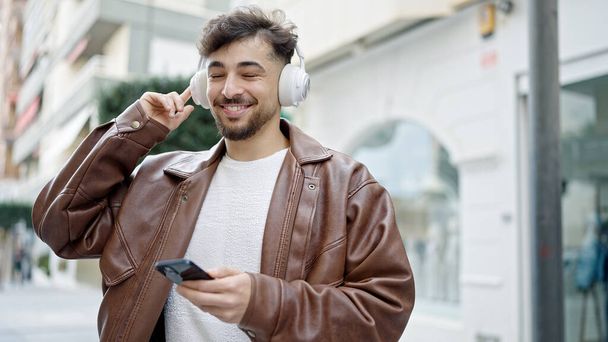 Junger arabischer Mann lächelt selbstbewusst, hört Musik und tanzt auf der Straße - Foto, Bild