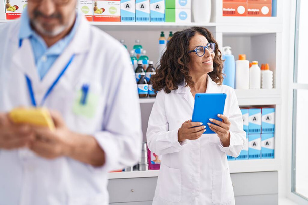 Man and woman pharmacists using touchpad and smartphone working at pharmacy - Foto, imagen