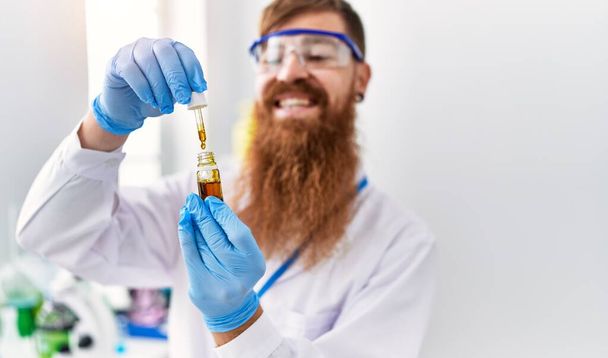 jovem ruiva homem vestindo cientista uniforme segurando reativo no laboratório - Foto, Imagem