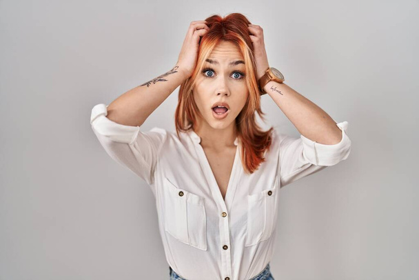 Young caucasian woman standing over isolated background crazy and scared with hands on head, afraid and surprised of shock with open mouth  - Valokuva, kuva
