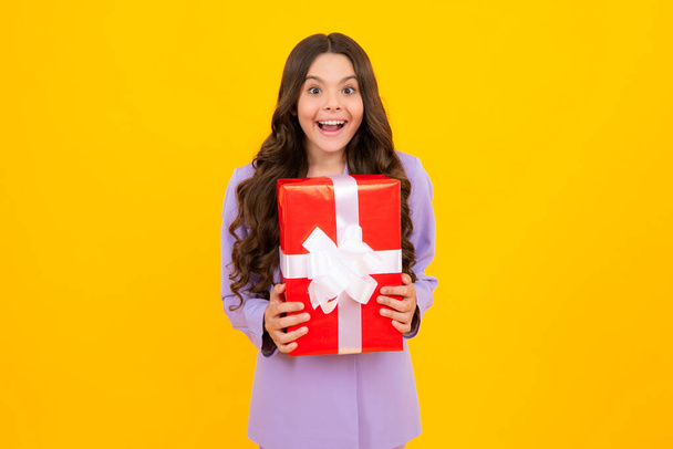 Teenager child holding gift box on yellow isolated background. Gift for kids birthday. Christmas or New Year present box. Amazed teen girl. Excited expression, cheerful and glad - Photo, Image