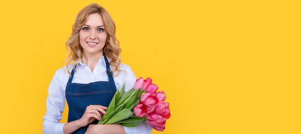 glad girl in apron with spring tulip flowers on yellow background. Woman isolated face portrait, banner with mock up copy space - Fotografie, Obrázek