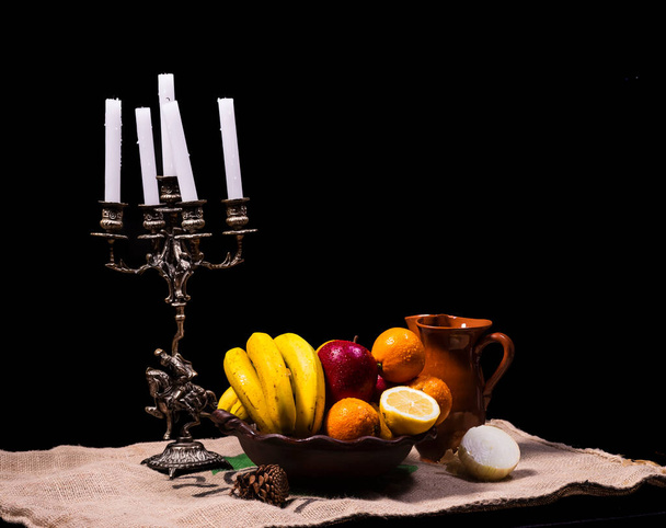 vida tranquila de fruto em um vaso de barro com um suporte de vela em um contexto escuro - Foto, Imagem