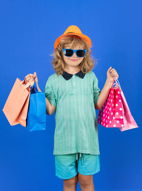 Moda çocuğu alışverişte. Alışveriş çantalı bir çocuğun portresi. Alışveriş torbaları tutan mutlu çocuk. Stüdyo resmi - Fotoğraf, Görsel