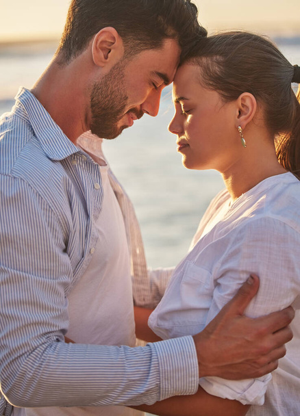 Couple, sunset and beach for love together on holiday or honeymoon. Man, woman and ocean in embrace for romance, during vacation, trip or travel by the sea in late summer sunlight show happiness. - Photo, Image